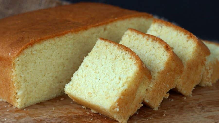 Fatias de um bolo caseiro retangular, com textura fofinha e cor dourada, sobre uma tábua de madeira