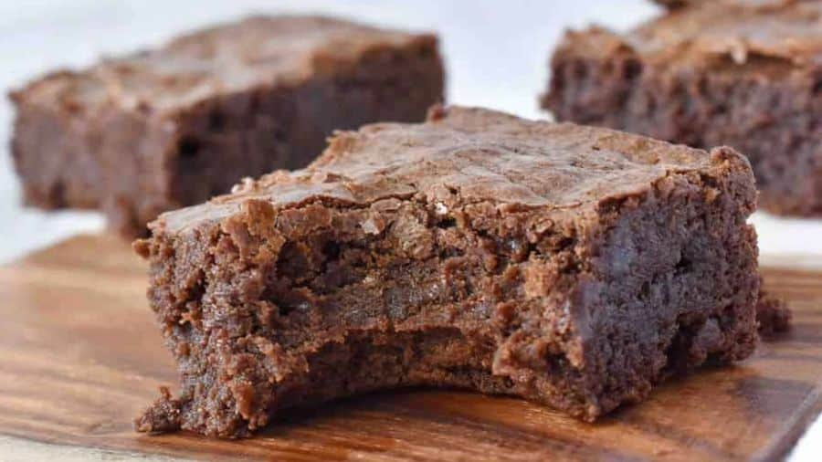 Close de um pedaço de brownie com interior denso e úmido, colocado sobre uma tábua de madeira