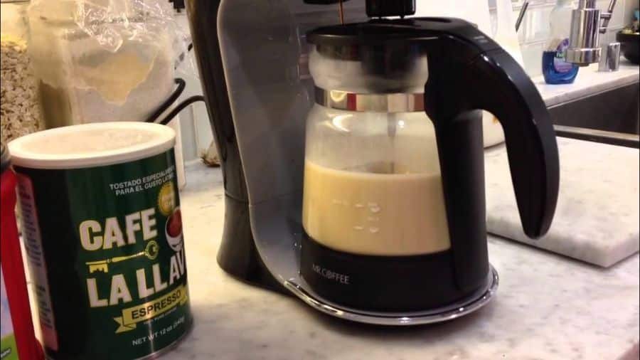 Cafeteira elétrica preparando café com leite, com uma lata de café expresso ao lado em uma bancada de cozinha