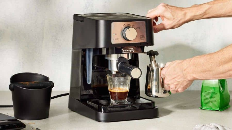 Máquina de café expresso com um espumador de leite sendo usado, preparando um café fresco em uma cozinha