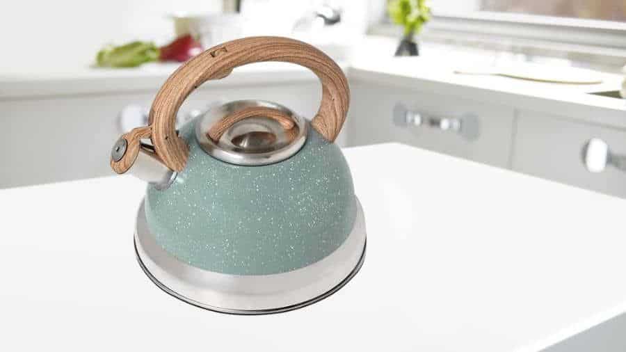 Chaleira com apito em inox na cor verde, com alça que imita madeira, sobre uma mesa de cozinha, usada como imagem destacada