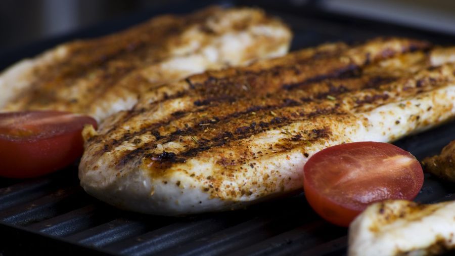 Filé de frango grelhado com temperos e fatias de tomate sobre uma grelha quente