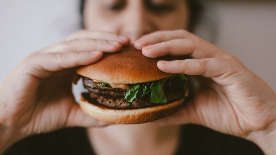 Pessoa segurando um hambúrguer com alface e carne grelhada, pronta para dar a primeira mordida