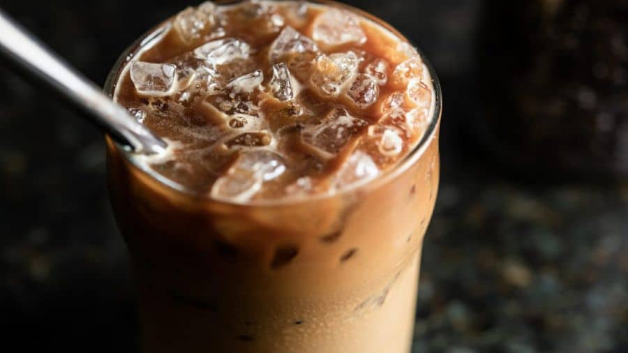 Close em copo de café gelado com leite e pedras de gelo, fundo escuro e foco na textura da bebida