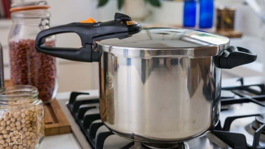 Panela de pressão inox sobre fogão aceso com grãos ao fundo