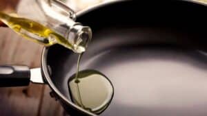 Óleo sendo despejado em frigideira antiaderente nova, usada como imagem destacada do artigo