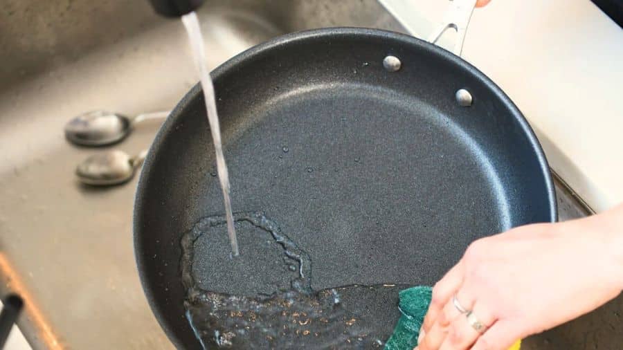 Pessoa lavando frigideira antiaderente com esponja macia e água corrente para preservar o revestimento