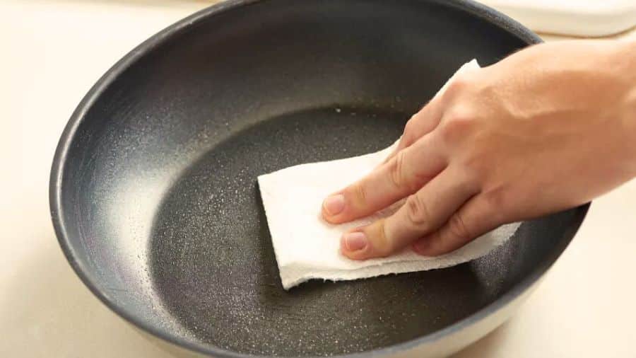 Mão passando óleo em frigideira com papel toalha para criar camada antiaderente antes do uso