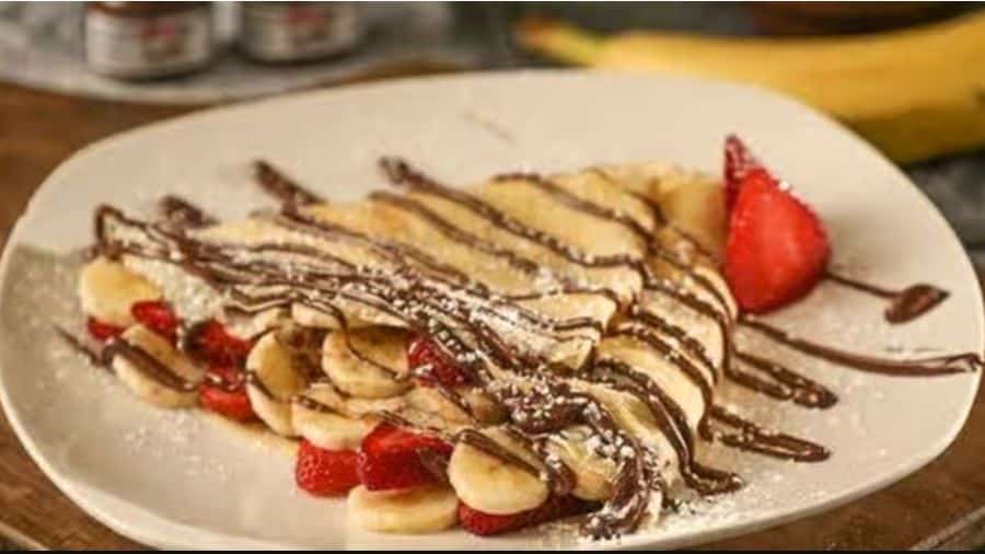 Tapioca doce recheada com banana e morango, coberto com calda de chocolate e açúcar de confeiteiro, usado como imagem ilustrativa do artigo