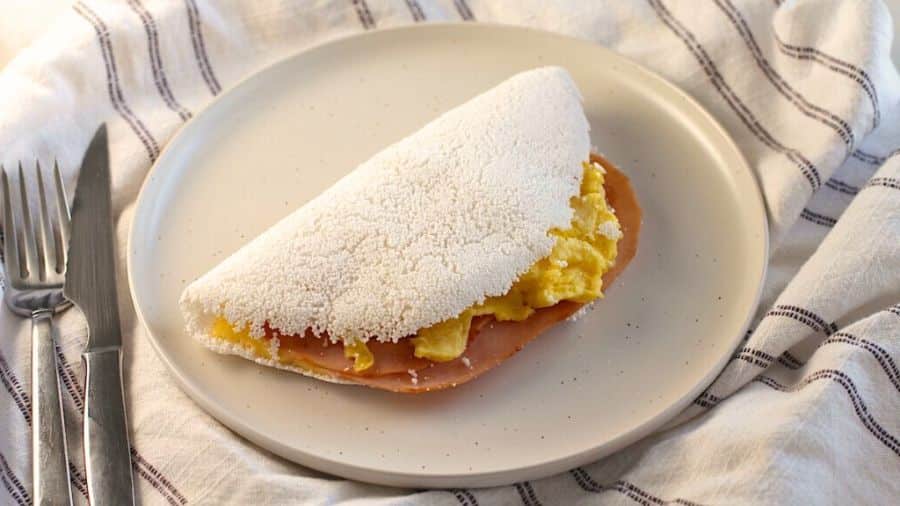 Tapioca com ovo mexido e fatias de presunto em prato branco, usada como imagem destacada do artigo