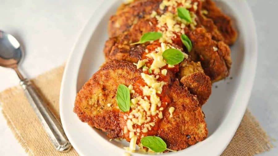 Tapioca de frango empanado coberta com molho vermelho, queijo picado e folhas frescas de manjericão, usados como imagem ilustrativa do artigo.