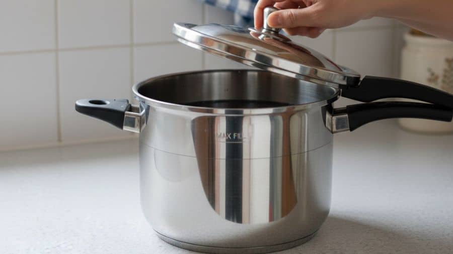 Panela de pressão sendo preenchida até o limite seguro com feijão e água, em cozinha comum